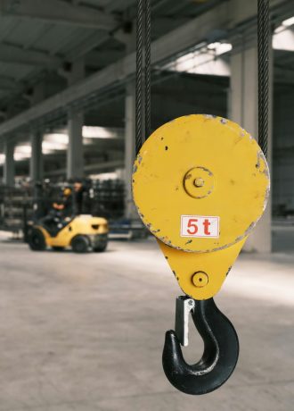 Closeup of a yellow industrial hook in a spacious factory with a focused background.